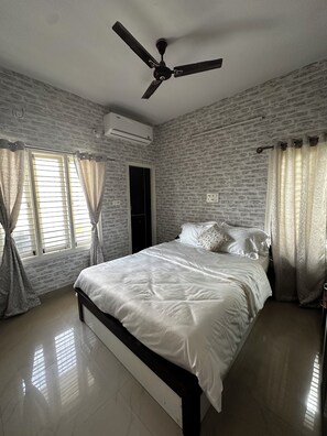 Une chambre à coucher comprenant un lit, un ventilateur de plafond, un appareil de climatisation et une fenêtre avec des rideaux.