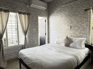 Ein Schlafzimmer mit Ziegelwand, einem Bett mit weißer Bettwäsche und einem Fenster mit Vorhängen.