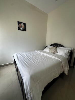 Un lit simple avec une couvre-lit blanche, une tête de lit noire et un seul coussin décoratif.