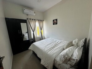 Une chambre à coucher comprenant un lit, une armoire, un miroir, une fenêtre avec des rideaux et un appareil de climatisation.