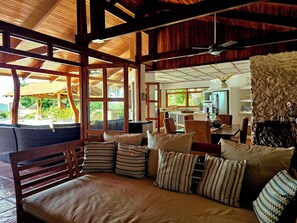 A spacious living area with a wooden ceiling, a sofa with patterned cushions, and a view of the outdoors through large windows. - Villa Bonita – Luxury Secluded Mountain Retreat in Costa Rica (Provincia de Guanacaste)
