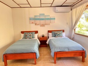 A room with two wooden beds, a wall-mounted air conditioner, and a beach-themed artwork. - Villa Bonita – Luxury Secluded Mountain Retreat in Costa Rica (Provincia de Guanacaste)