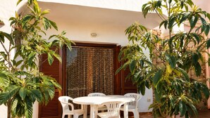 An outdoor patio with a round table and four white plastic chairs, surrounded by potted plants and a wooden door with a patterned curtain. - Residence Domenique | Three-room apartment for 4 guests (Tanaunella)