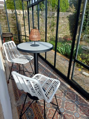 Una mesa redonda con una lámpara de fibras vegetales, dos sillas blancas de mimbre y vistas a un jardín a través de amplias ventanas.