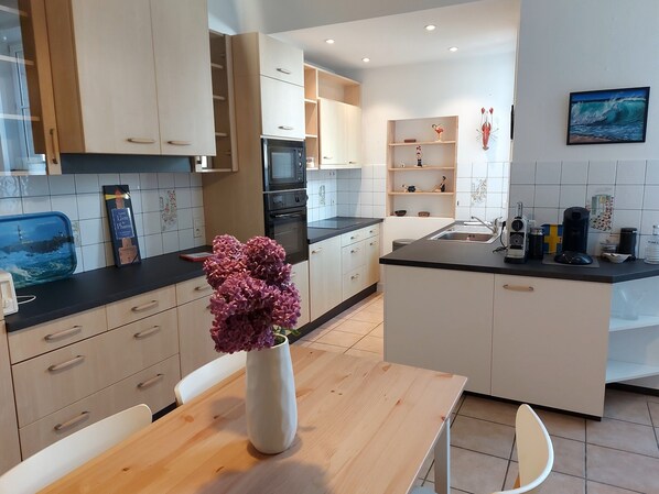 Una cocina moderna con armarios blancos, una isla central y un florero con flores moradas sobre la mesa.