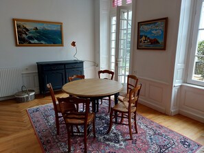 A dining room with a round table, four chairs, a patterned rug, a dark blue cabinet, and two paintings on the walls. - Apartment Quimper hyper-centre, 3 bedrooms (Quimper)