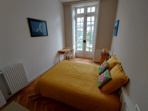 A bedroom with a bed, a chair, a desk, a radiator, and a door leading to a balcony. - Apartment Quimper hyper-centre, 3 bedrooms (Quimper)