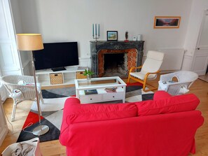 A living room with a red sofa, a television, a fireplace, and a white armchair. - Apartment Quimper hyper-centre, 3 bedrooms (Quimper)