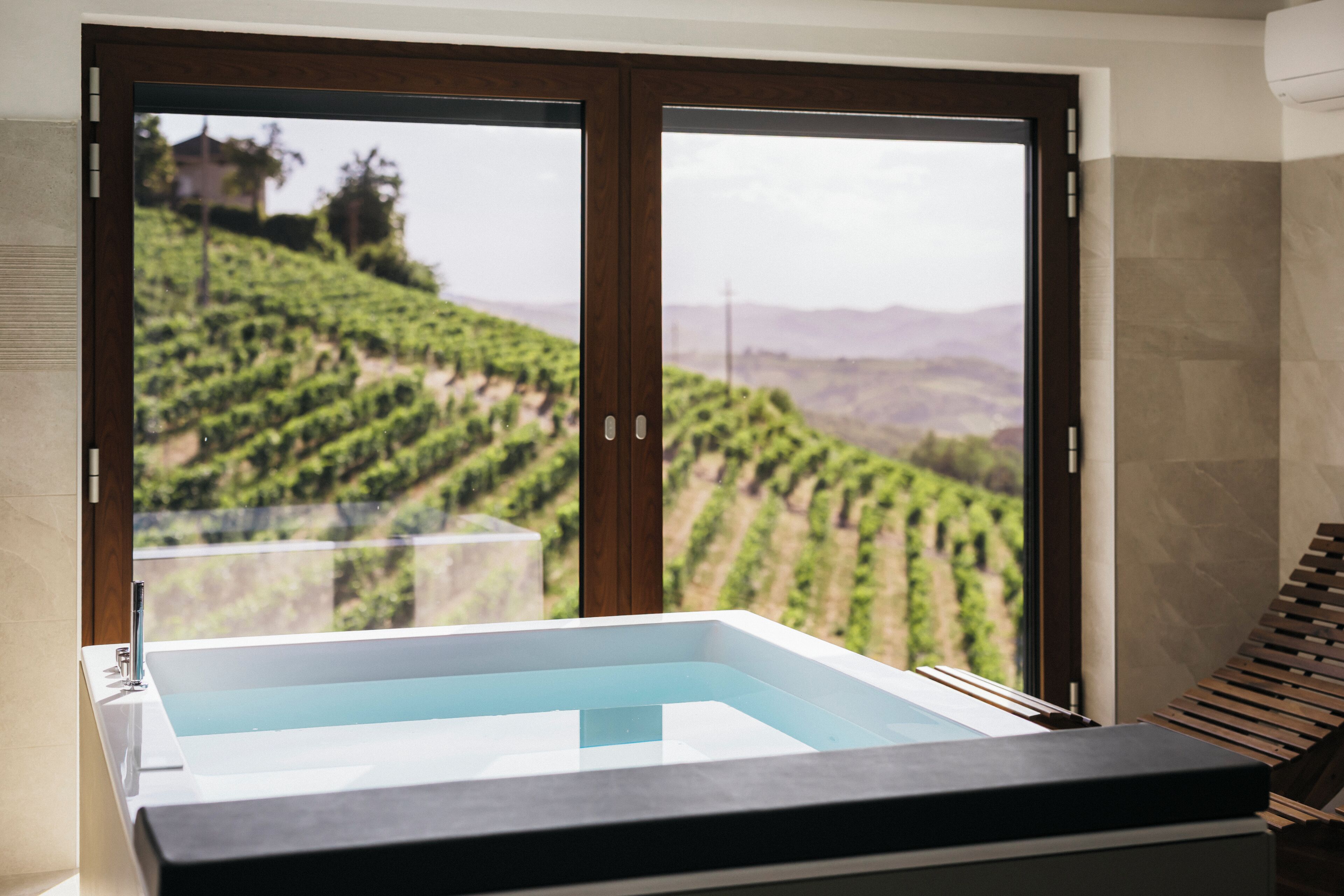 Ein Wellnessbereich mit Whirlpool und Blick auf einen Weinberg durch große Schiebetüren.