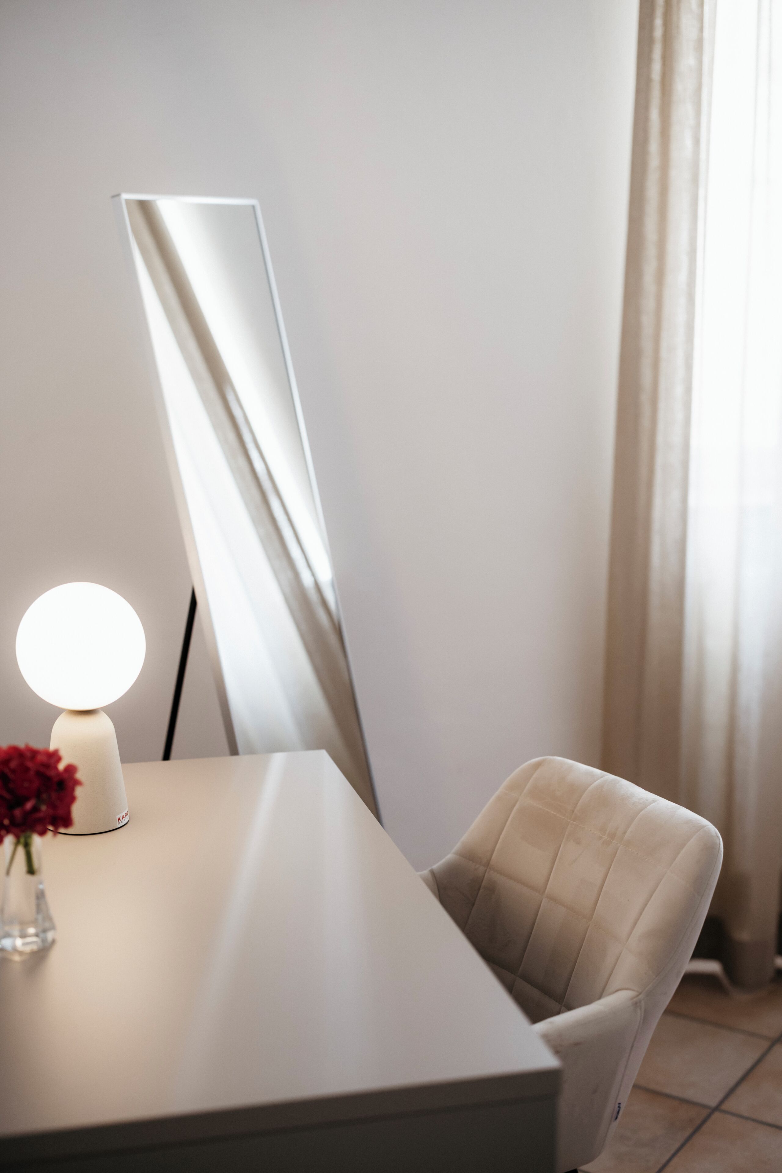 A modern room with a white desk, a chair, a floor lamp, and a large mirror.