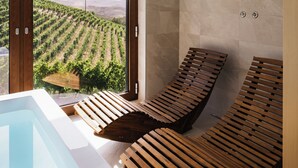 A spa area with a hot tub, wooden loungers, and a view of a vineyard through a large window. - Private Relax Apartment: Sauna and Mini Pool (Piemonte)