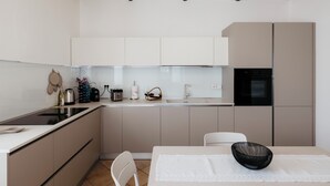 A modern kitchen with white cabinets, a black refrigerator, and a dining area with a white table and chair. - Private Relax Apartment: Sauna and Mini Pool (Piemonte)