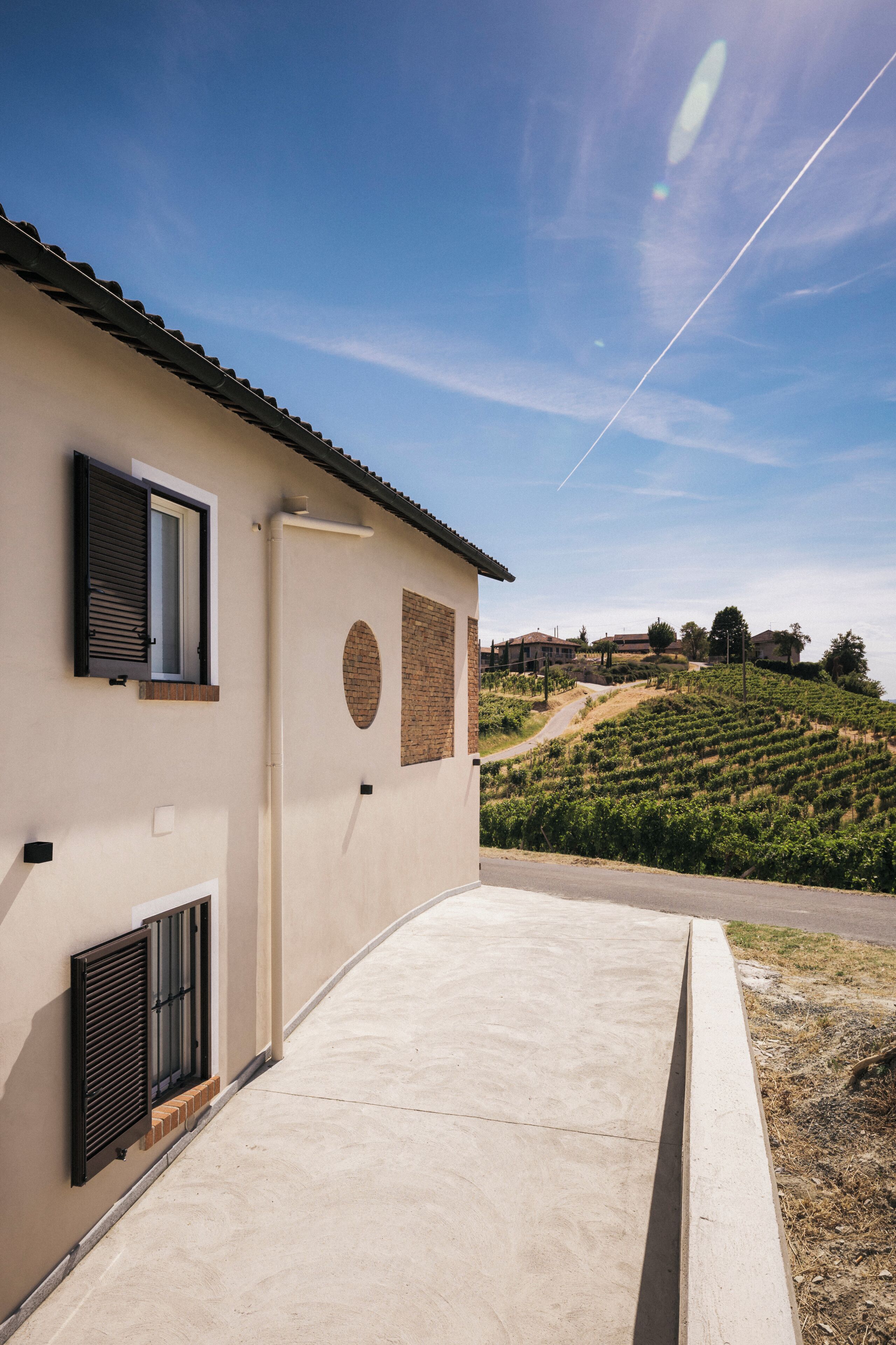 Un bâtiment doté d’un toit plat, d’une terrasse en béton et, en arrière-plan, d’un vignoble en pente.