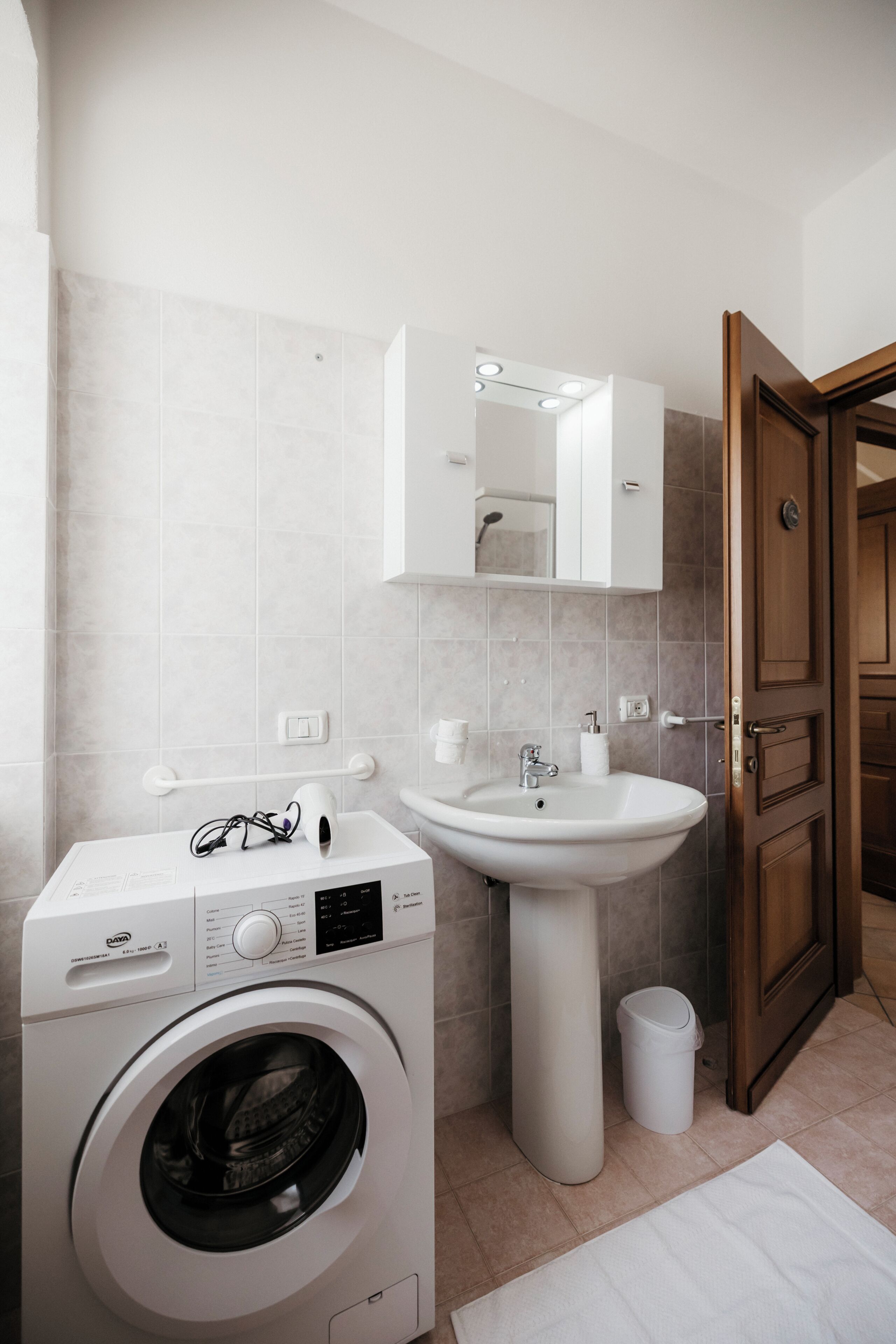 Une petite salle de bain équipée d’un lave-linge, d’un évier et d’une porte en bois.