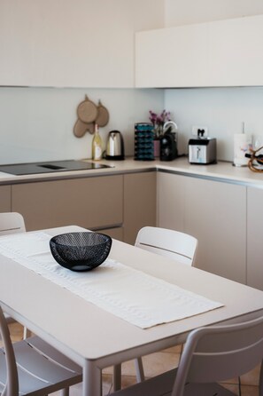 Ett modernt kök med vita skåp, ett matbord med en vit bordsduk och en svart, flätad skål på bordet.