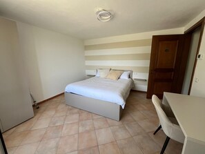 A bedroom with a bed, a chair, a desk, and a door. - Private Relax Apartment: Sauna and Mini Pool (Piemonte)