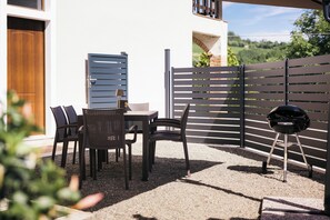 An outdoor patio area with a table and chairs, a barbecue grill, and a wooden door. - Private Relax Apartment: Sauna and Mini Pool (Piemonte)