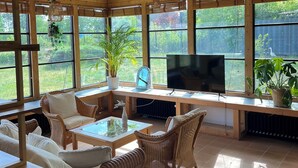 A sunlit room with large windows, wicker furniture, a flat-screen TV, and potted plants. - Fantastic vacation home close to nature with sauna (Amelinghausen)