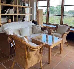 A living room with a white sofa, two wicker chairs, a glass coffee table, and a bookshelf filled with books and decorative items. - Fantastic vacation home close to nature with sauna (Amelinghausen)