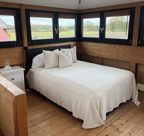 A bedroom with a wooden headboard, a bed with white bedding, a bedside table with a lamp, and large windows with blinds. - Fantastic vacation home close to nature with sauna (Amelinghausen)