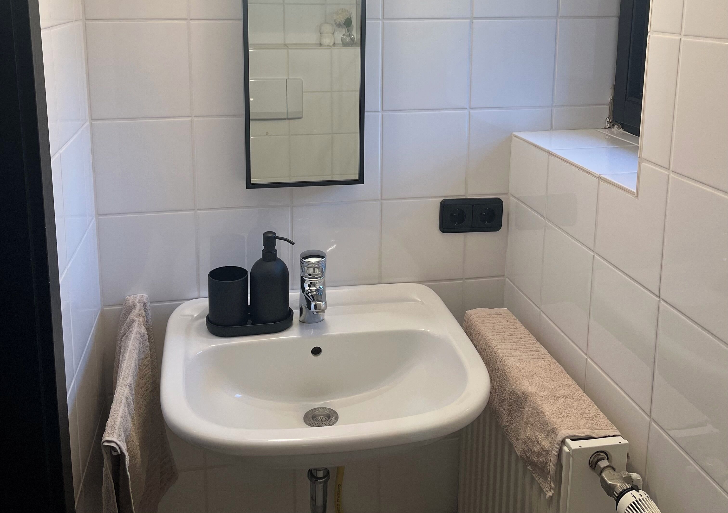 Ein Badezimmer mit einem weißen Waschbecken, einem Spiegel, einem Handtuchhalter und einem Handtuch.
