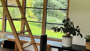 A wooden interior with large windows, a ladder, a potted plant, and a black speaker. - Fantastic vacation home close to nature with sauna (Amelinghausen)