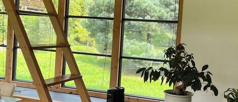 A wooden interior with large windows, a ladder, a potted plant, and a black speaker.