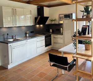 A modern kitchen with white cabinets, a black stove, and a wooden dining table with chairs. - Fantastic vacation home close to nature with sauna (Amelinghausen)