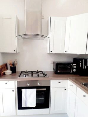 Een moderne keuken met witte kastjes, een gasfornuis, een oven, een broodrooster en een afzuigkap.