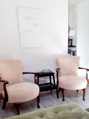 Twee fauteuils, een bijzettafeltje met een glazen asbak, en een lijst met een foto aan de muur.