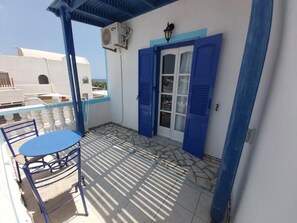 Varanda com mesa e cadeiras, porta com persianas azuis e chão de azulejos.