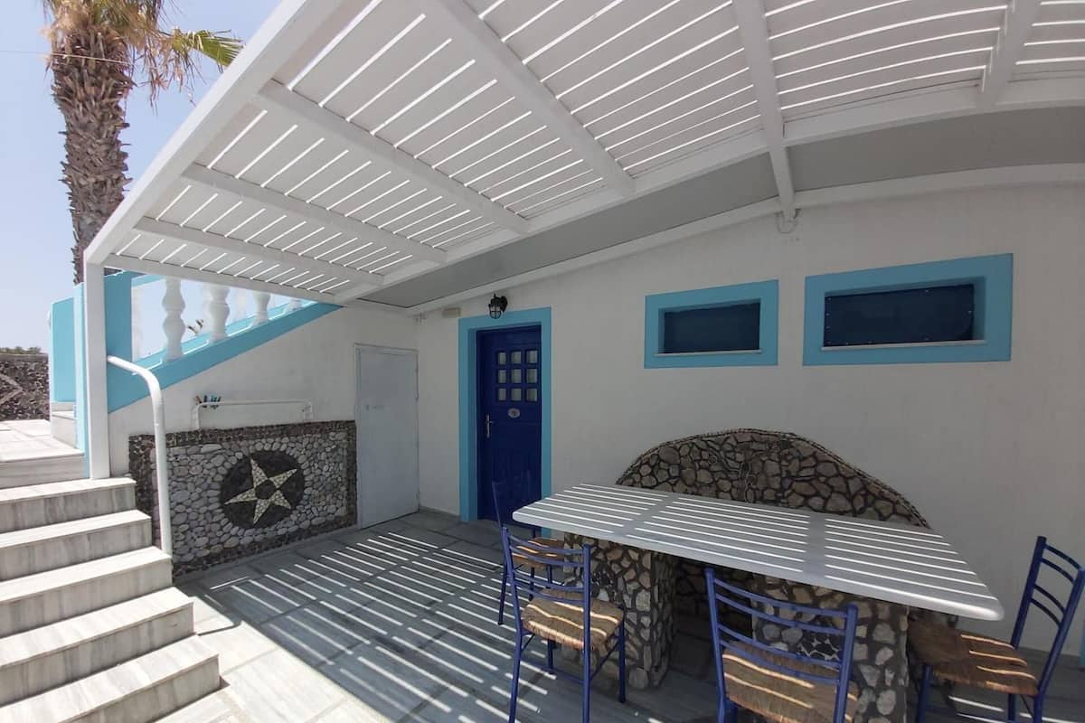 A covered outdoor area with a stone wall, a blue door, and a table with chairs.