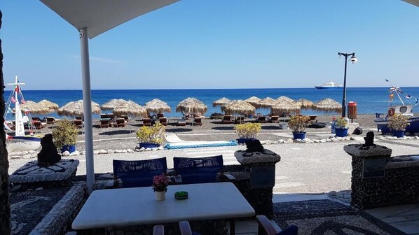 Um terraço à beira-mar com mesas ao ar livre, guarda-sóis e vista para o mar.