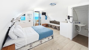 Quarto com cama, banheiro com pia e vista para o mar.
