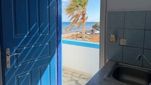 Uma porta azul que dá para uma varanda com vista para o mar e uma palmeira.