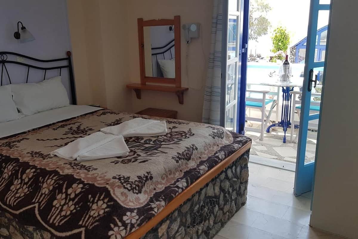 A bed with a patterned bedspread and two folded towels, a bedside lamp, a mirror, and a view of an outdoor pool area.