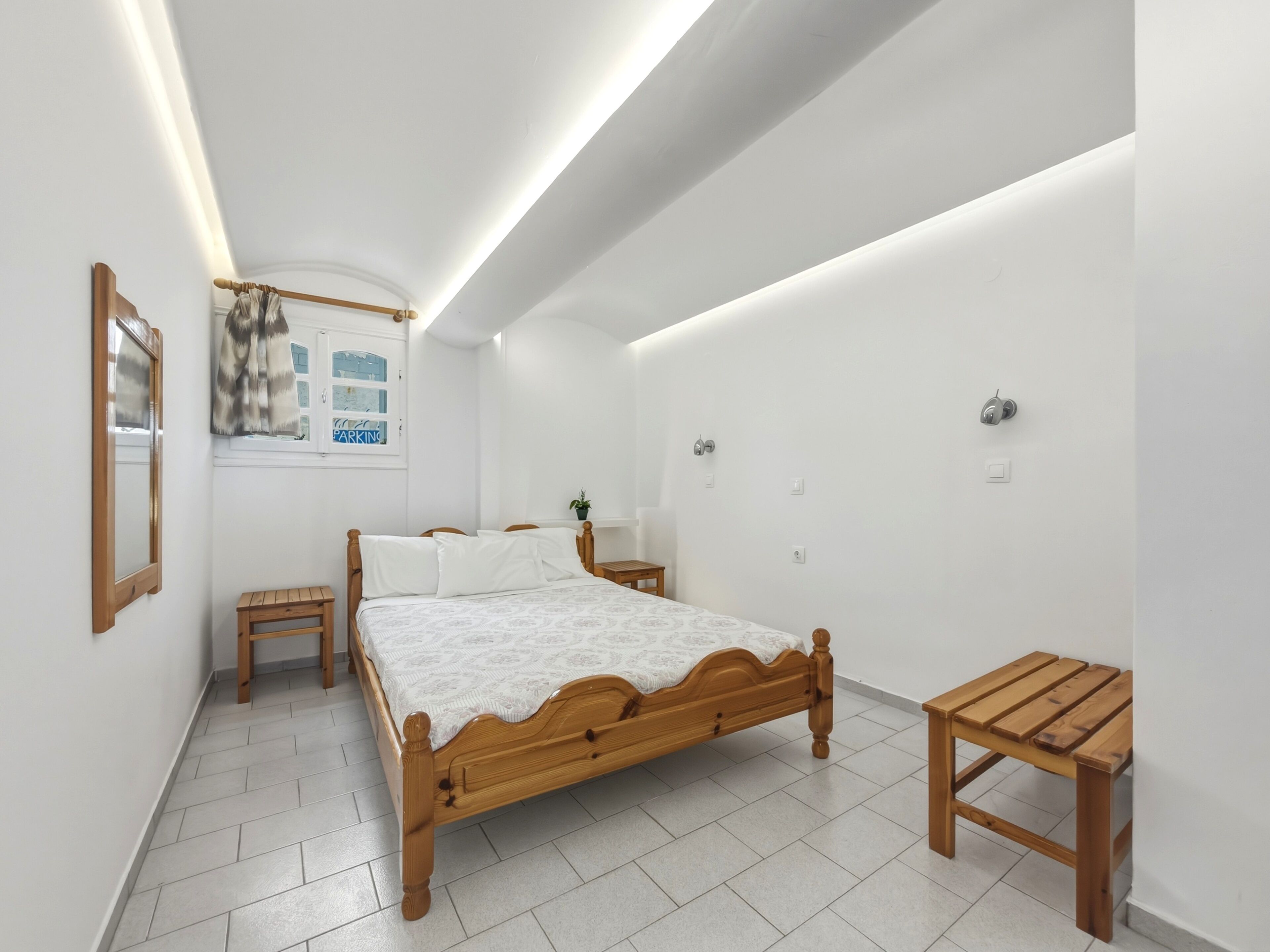 Quarto com cama de madeira, mesa de cabeceira, mesa lateral, uma pequena mesa de madeira e uma janela com vista para o exterior.
