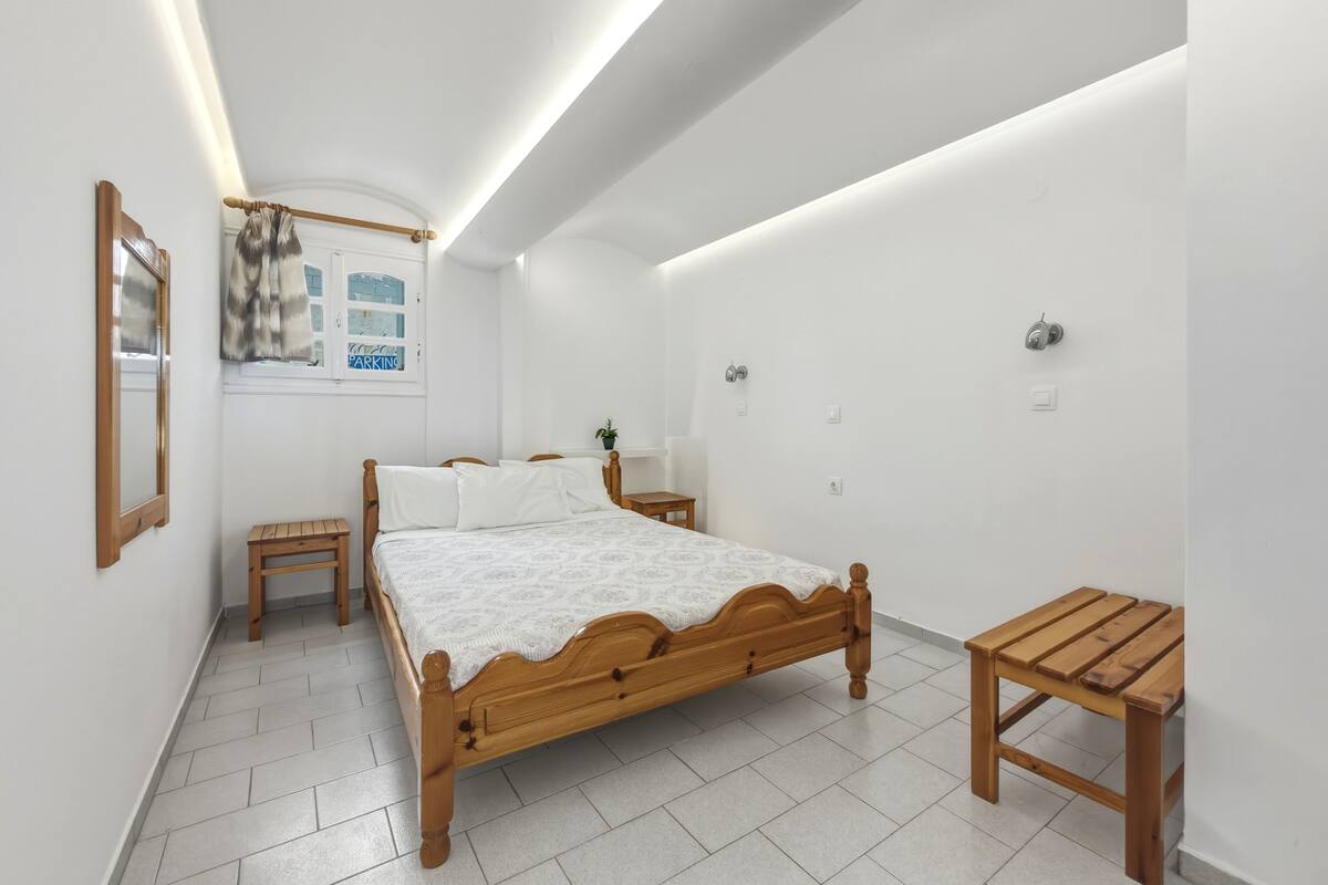 Un dormitorio con cama de madera, una mesita de noche, una pequeña mesa de madera y una ventana con vistas al exterior.