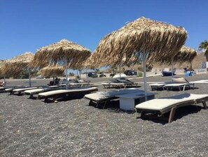 Uma praia com espreguiçadeiras e guarda-sóis de palha.