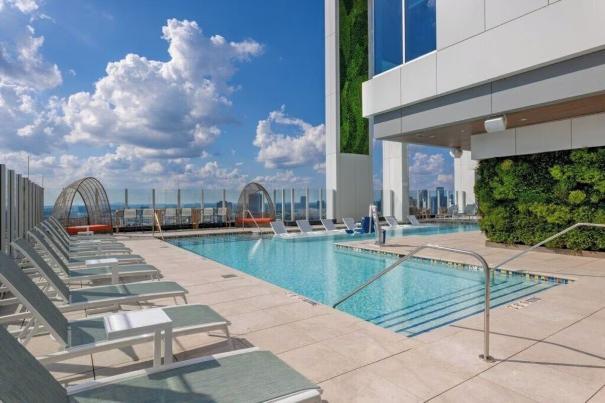 Une piscine sur le toit, dotée de chaises longues, d’une balustrade en verre et offrant une vue sur le panorama urbain.
