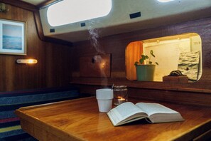 A wooden bench with a book and a cup, a mirror reflecting a plant and a window, and a small candle on the bench.