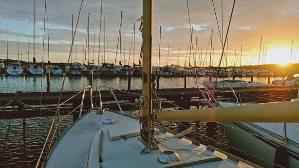 Een jachthaven met meerdere boten afgemeerd, een heldere lucht en een zonsondergang.
