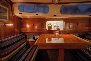 A compact, well-lit interior with a wooden table, cushioned seating, and a small window displaying a plant.