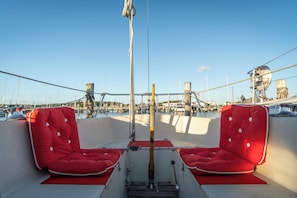 Un pont de bateau avec deux siĂšges rouges rembourrĂ©s, un volant et une vue sur une marina oĂč se trouvent d'autres bateaux.