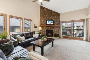 Ein Wohnzimmer mit Steinwand, Kamin, Fernseher und einem Balkon mit Glastüren.