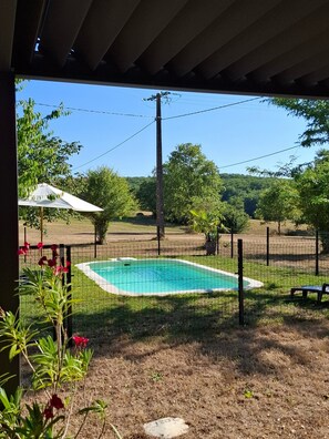 Ein Garten mit Swimmingpool, überdachter Terrasse und umzäunter Grundstück.