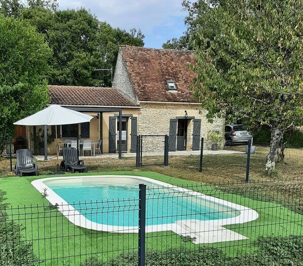 Ein Garten mit Swimmingpool, einem Steinhaus und einem umzäunten Bereich mit Gartenmöbeln.