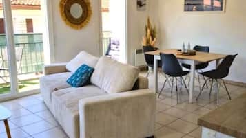 A living room with a sofa, a dining table with chairs, a window with a view, and a wall-mounted decorative item.