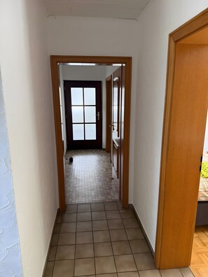 A hallway with a tiled floor, a door with frosted glass panels, and a view into another room.