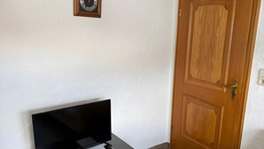 A room with a wooden door, a black TV on a table, a white couch, and a clock on the wall.